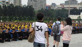 '大陆及来自各地的游客为场中七千多名学员的盛大场面所吸引，有的拿起相机拍照留念。'