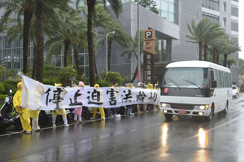 二十三日台风袭台，强卫车队至台中市裕元花园酒店，法轮功学员顶着强风暴雨拉着横幅告诉强卫：“停止迫害法轮功。”