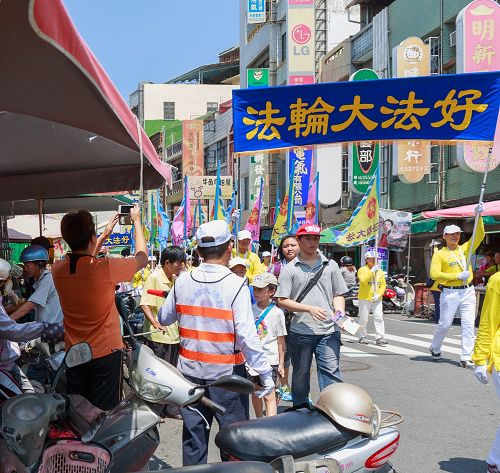 不少民众远远听到法轮功洪法队伍鼓乐声，早已聚集路旁等待队伍的到来，高举着手机、相机拍照留念。