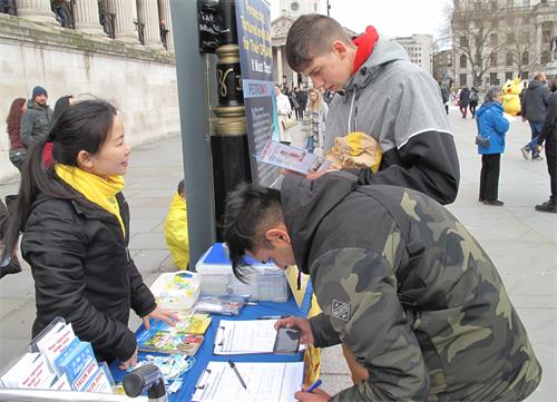 图6：二零二零年三月七日，在特拉法加广场，两个大学生丹尼斯（Denis）和马里斯彭（Marispen）签名支持法轮功反迫害。