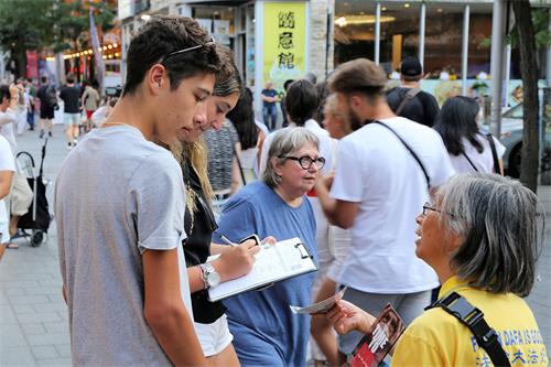 图7:二零二二年七月十九日，魁北克部分法轮功学员在蒙特利尔唐人街举行烛光夜悼。图为现在民众在制止迫害请愿书上签字。